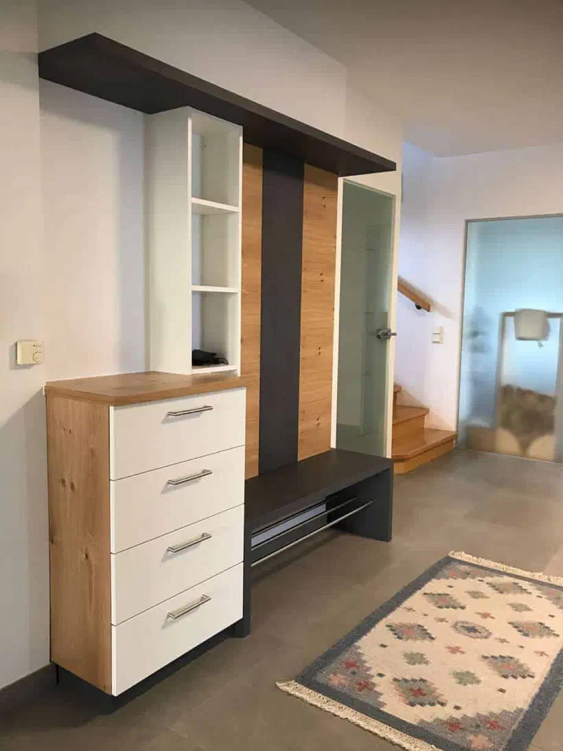 Garderobe mit weißen Laden, heller Holzrückwand mit dunklem Streifen und dunkler Sitzbank mit Schuhstangen